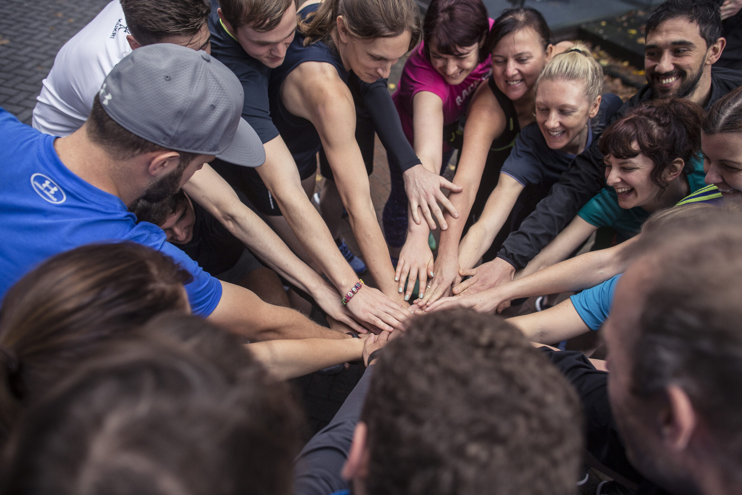 Photo from an Under Armour Show Trial Event in Manchester, showing a large group of people about to go on an organised run all putting their hands together to bolster their confidence before setting off